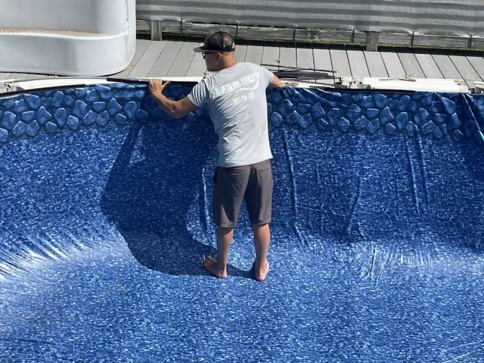 Crew member in a Hampton Pool Services shirt fitting the liner bead into the pool's top track