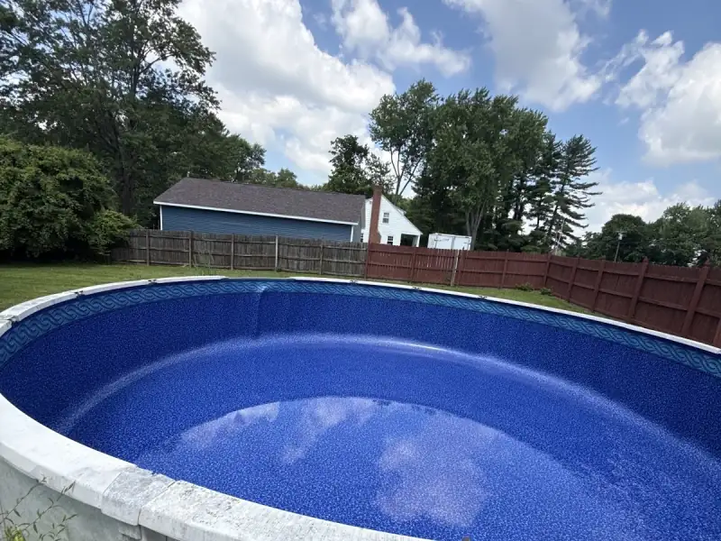 Round above-ground pool in a fenced backyard with a fresh blue liner